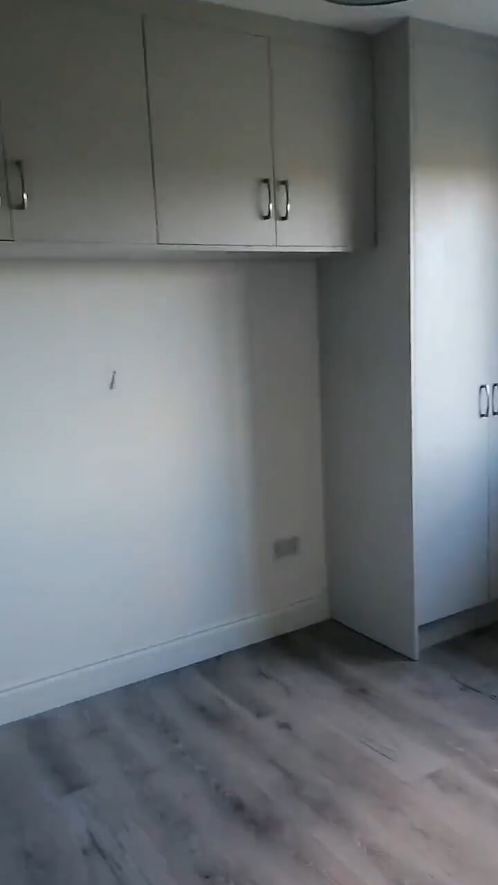 a master bedroom containing grey wardrobes surrounding where the bed would be placed and grey laminate flooring